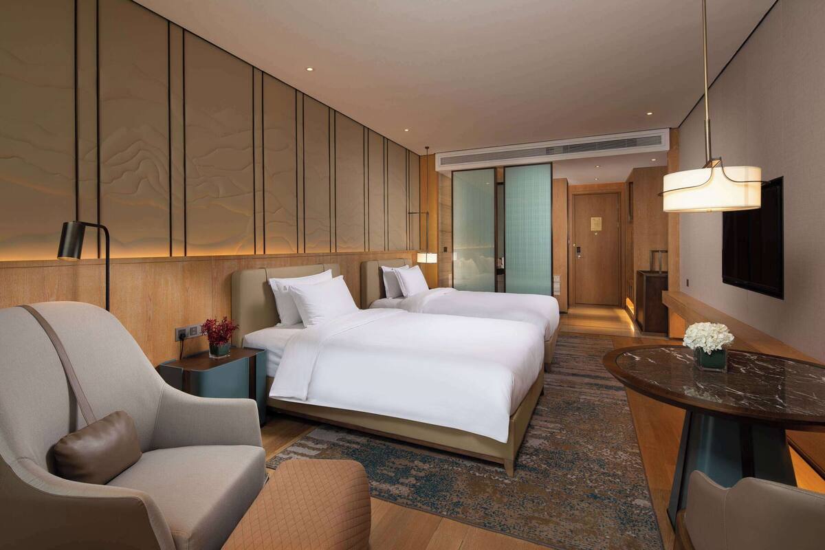 A hotel room with a large bed, a desk, a chair, and a TV.