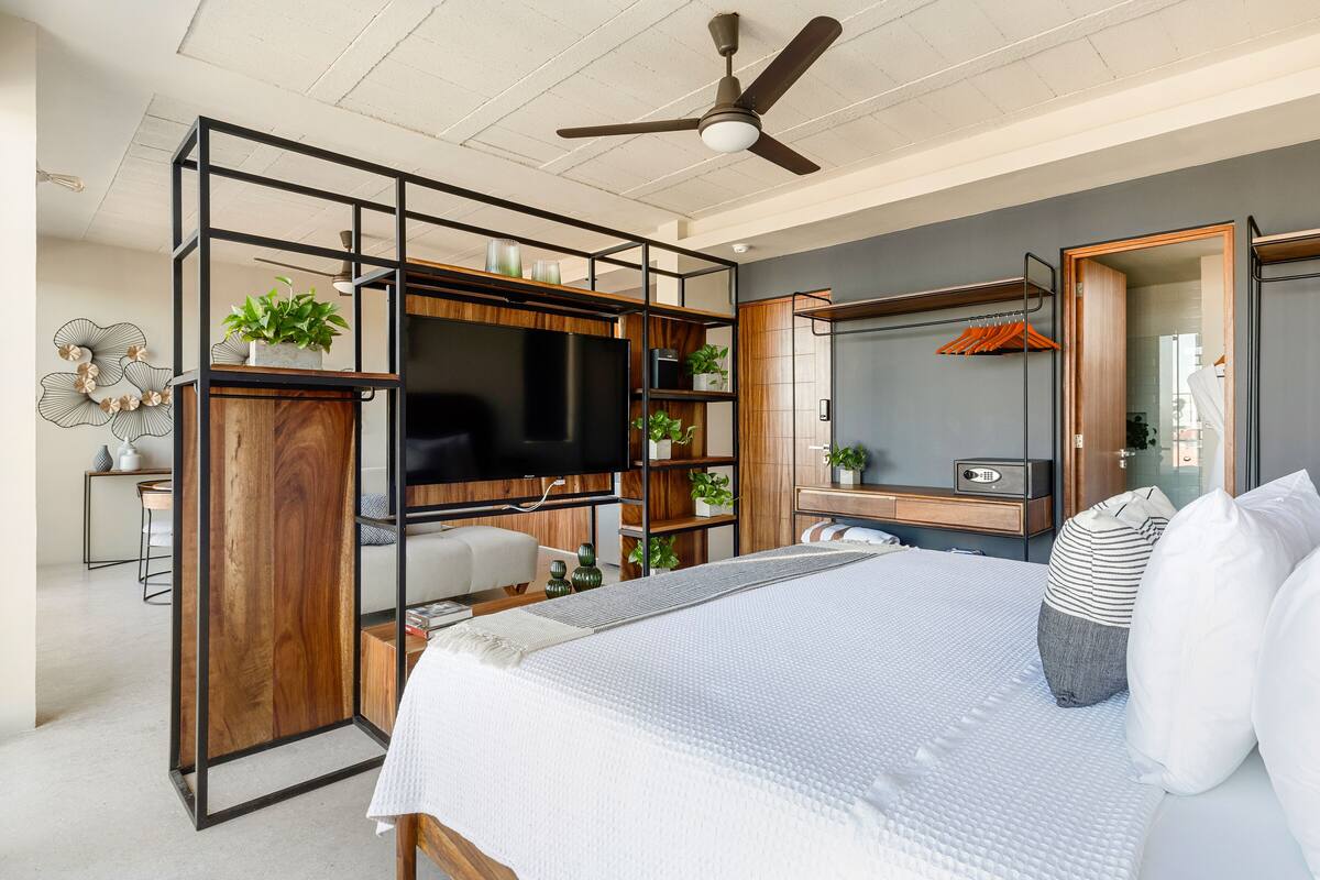 A modern bedroom with a large bed, a TV mounted on a wooden wall, and a ceiling fan.