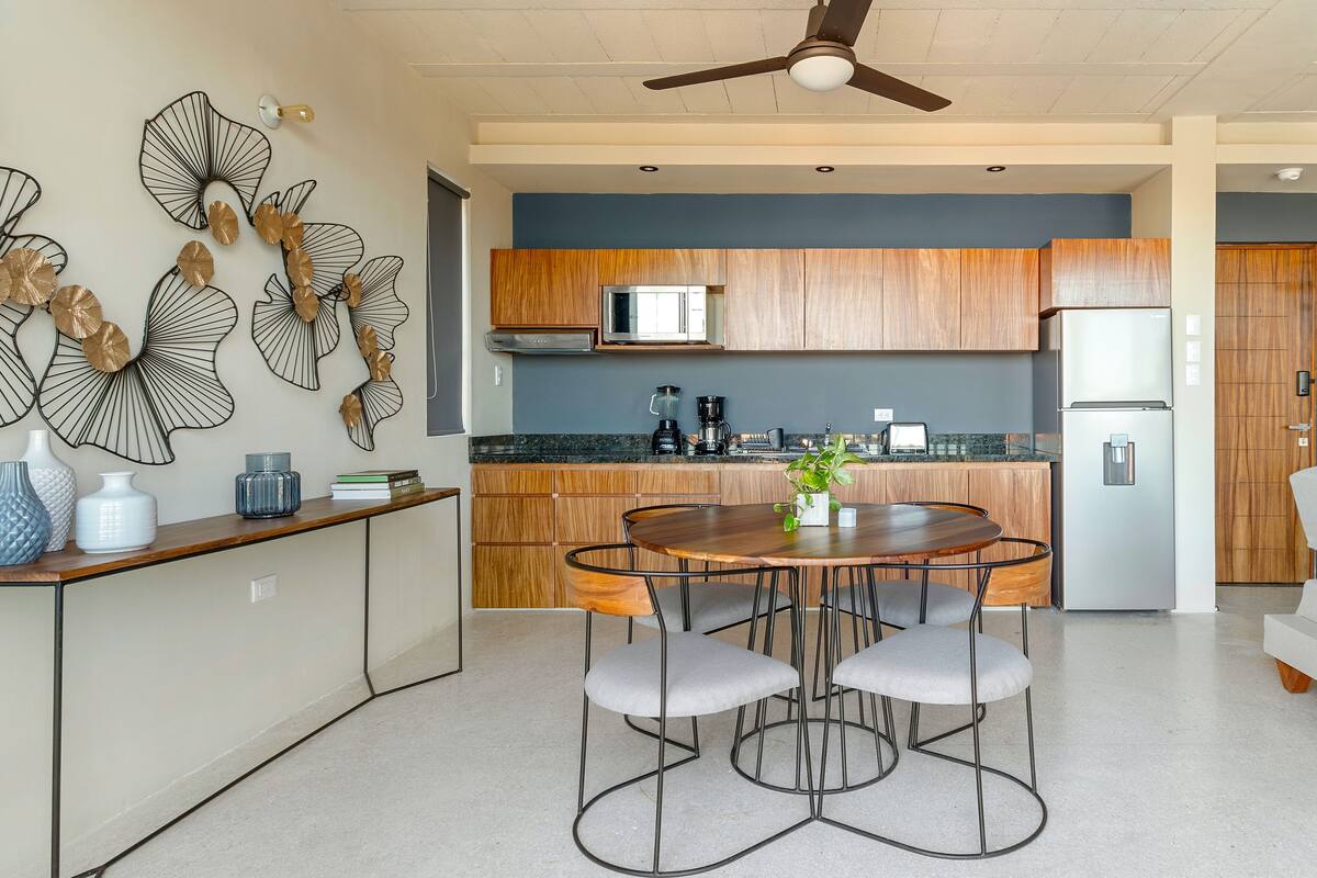 A modern kitchen with wooden cabinets, a stainless steel refrigerator, and a dining area with a round table and four chairs.