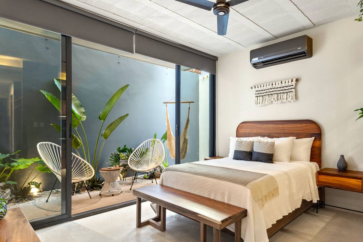 A modern bedroom with a large bed, a wooden bench, and a hammock.
