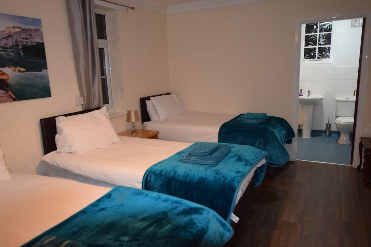 A hotel room with two beds, a nightstand, a window with curtains, and a bathroom visible through an open door.