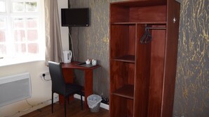 A room with a wooden desk, a chair, a television mounted on the wall, and a large wooden wardrobe. - Watling Inn (Nuneaton)