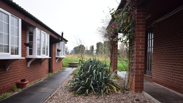 A narrow pathway flanked by brick buildings with white-framed windows and a small garden area with gravel and plants. - Watling Inn (Nuneaton)