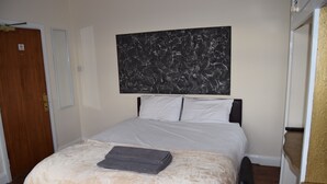 A hotel room with a bed, a large abstract painting on the wall, and a wooden door. - Watling Inn (Nuneaton)