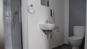 A modern bathroom with a glass shower enclosure, a white sink with a chrome faucet, and a toilet. - Watling Inn (Nuneaton)