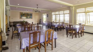 A dining area with multiple tables and chairs, a chandelier, and large windows with bars. - SPOT ON 1896 Hotel Mahkota Pantai (Pelabuhan Ratu)