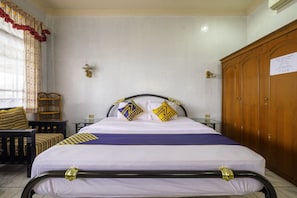 A neatly arranged hotel room with a bed, a wooden wardrobe, a small table, and a chair. - SPOT ON 1896 Hotel Mahkota Pantai (Pelabuhan Ratu)