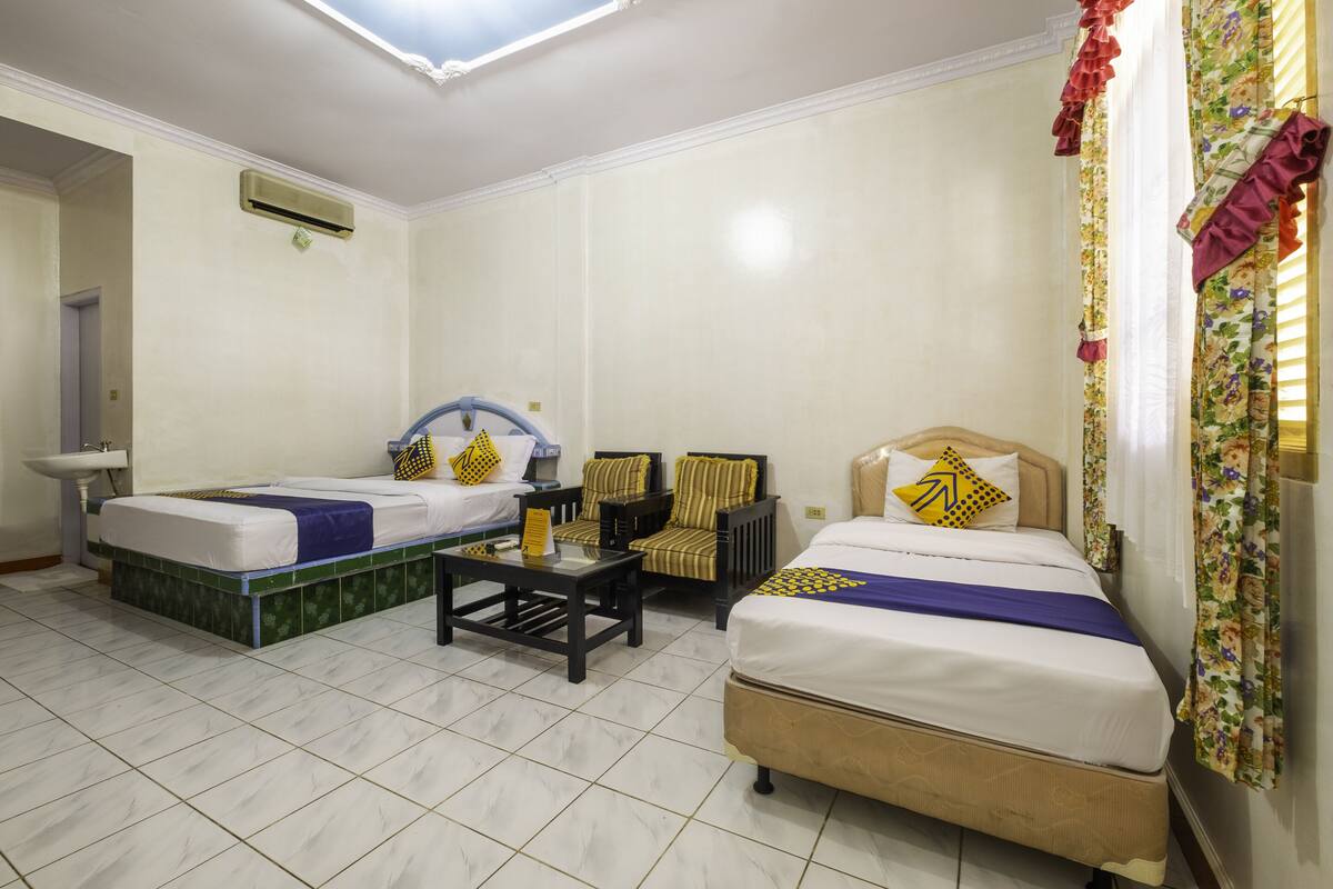 A hotel room with two beds, a small table, and a chair. There is a sink and an air conditioning unit on the wall.