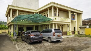 A hotel with a large entrance, two parked cars, and a covered area with columns. - SPOT ON 1896 Hotel Mahkota Pantai (Pelabuhan Ratu)