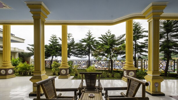 A covered outdoor seating area with a view of palm trees and a fence. - SPOT ON 1896 Hotel Mahkota Pantai (Pelabuhan Ratu)
