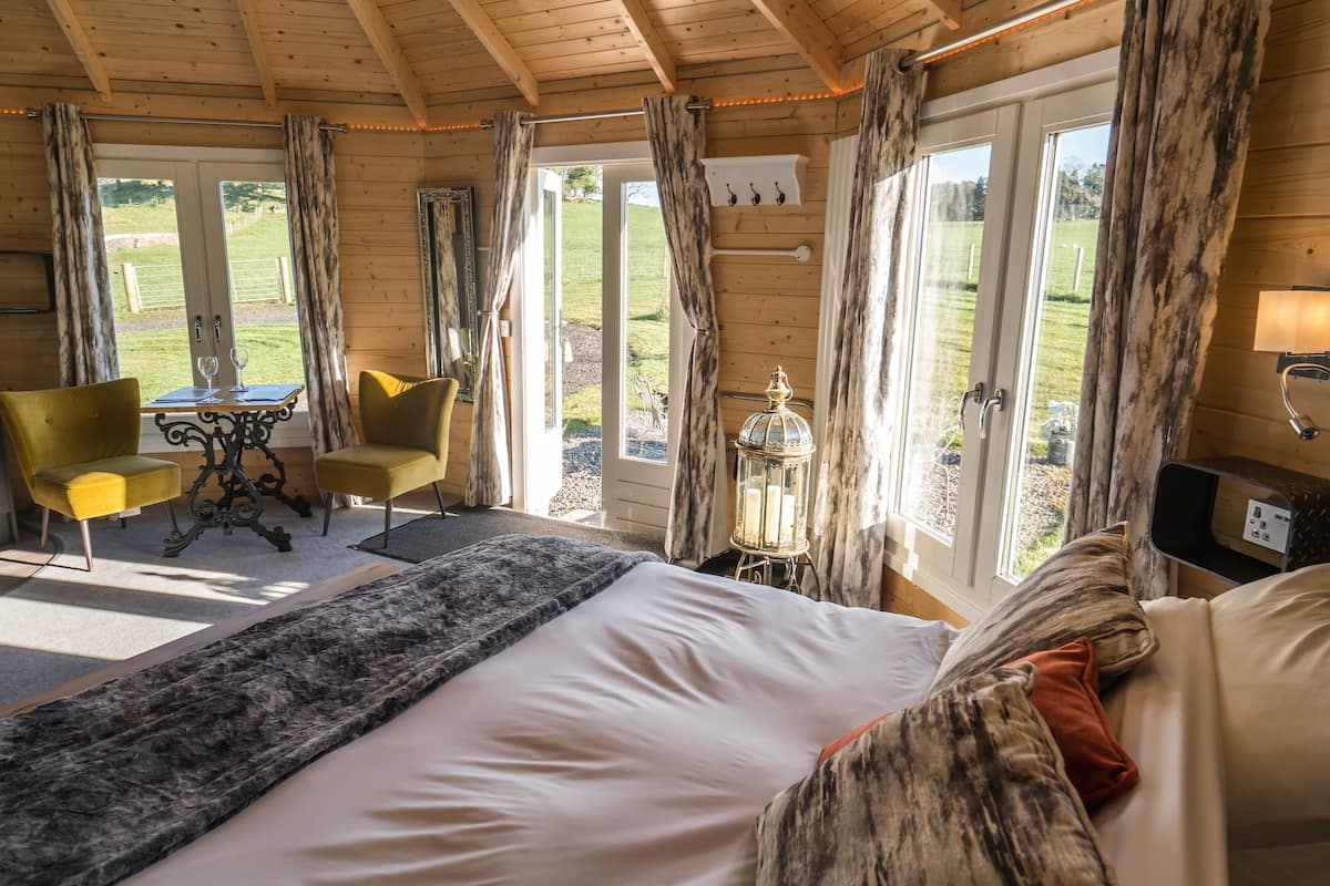 A wooden room with a bed, a table with chairs, and a view of the outdoors.