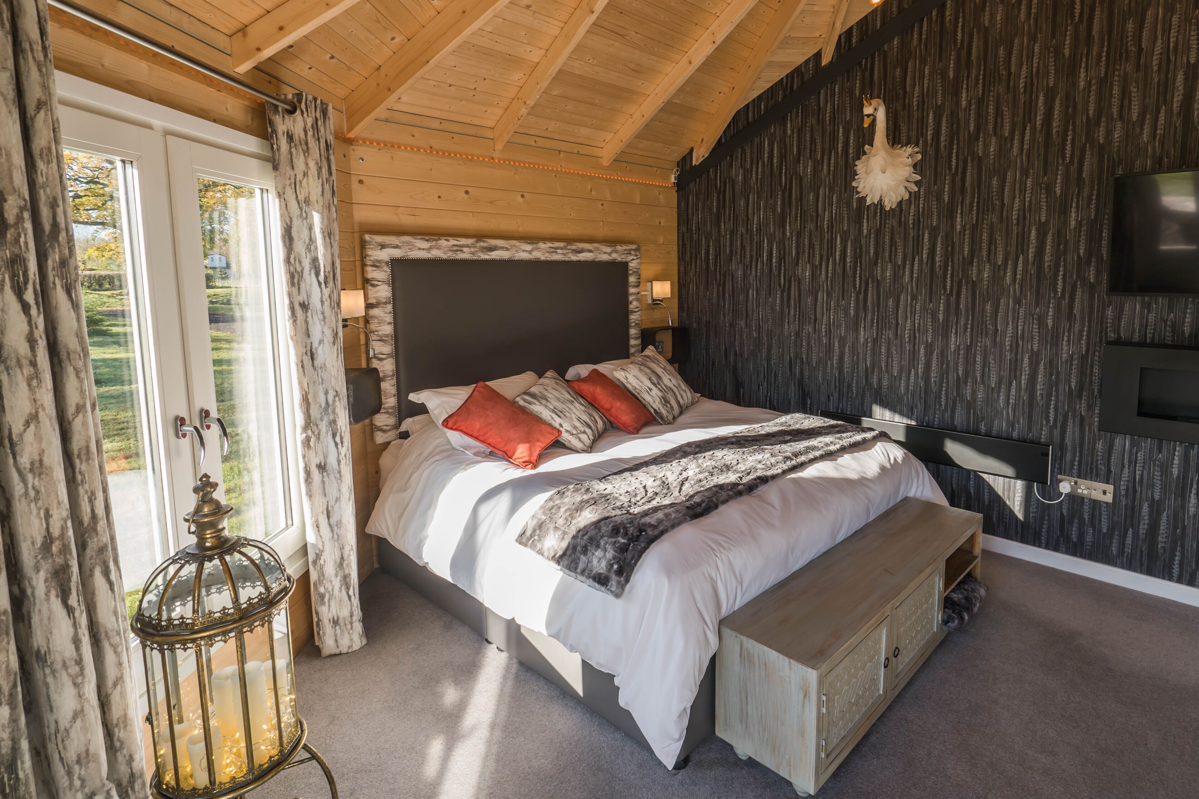 Ein Schlafzimmer mit einem großen Bett, einem Holzkopfteil, einem an der Wand montierten Fernseher und einem Fenster mit Vorhängen.