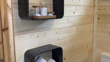 A wooden bathroom with two black shelves, one holding toiletries and the other towels.