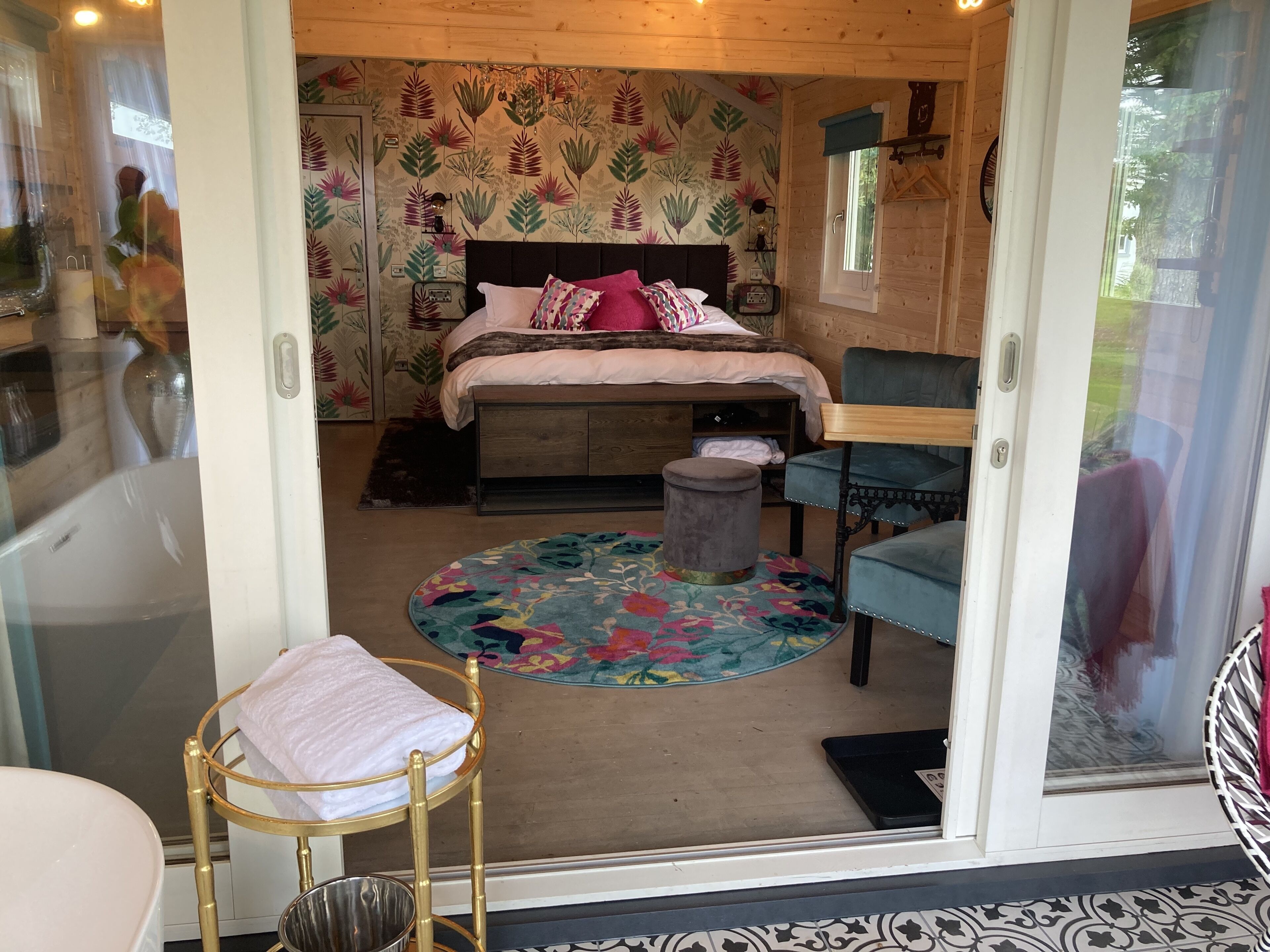 Un dormitorio con una cama, un tapete redondo, un taburete, una silla y una ventana.
