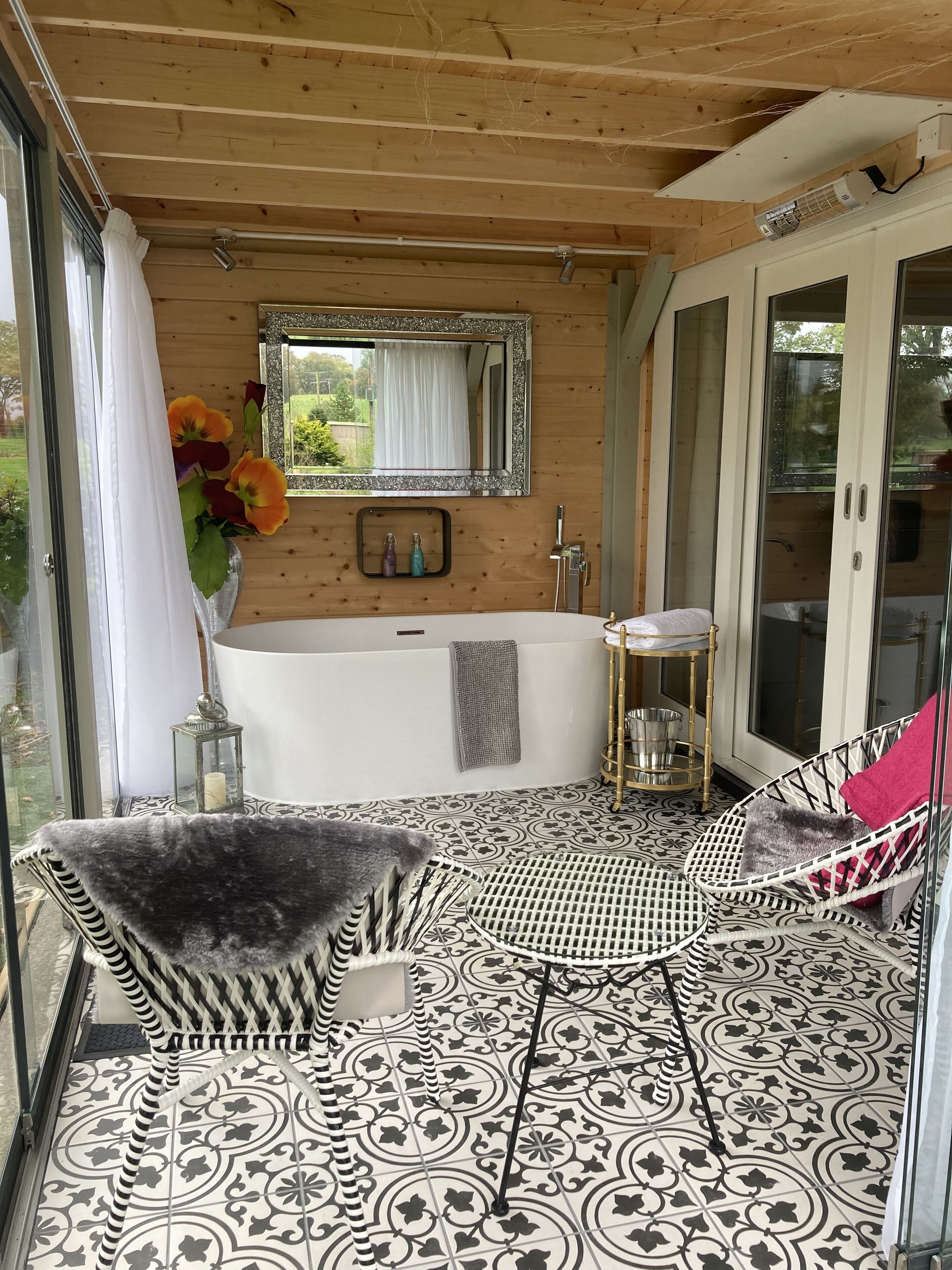 A bathroom with a freestanding bathtub, a mirror above it, and a window with curtains.