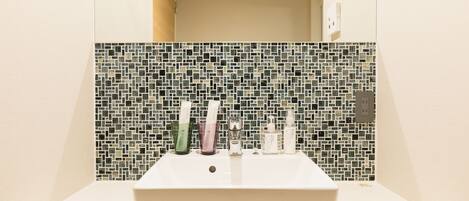 A bathroom with a white sink, a tiled backsplash, and toiletries on the counter.