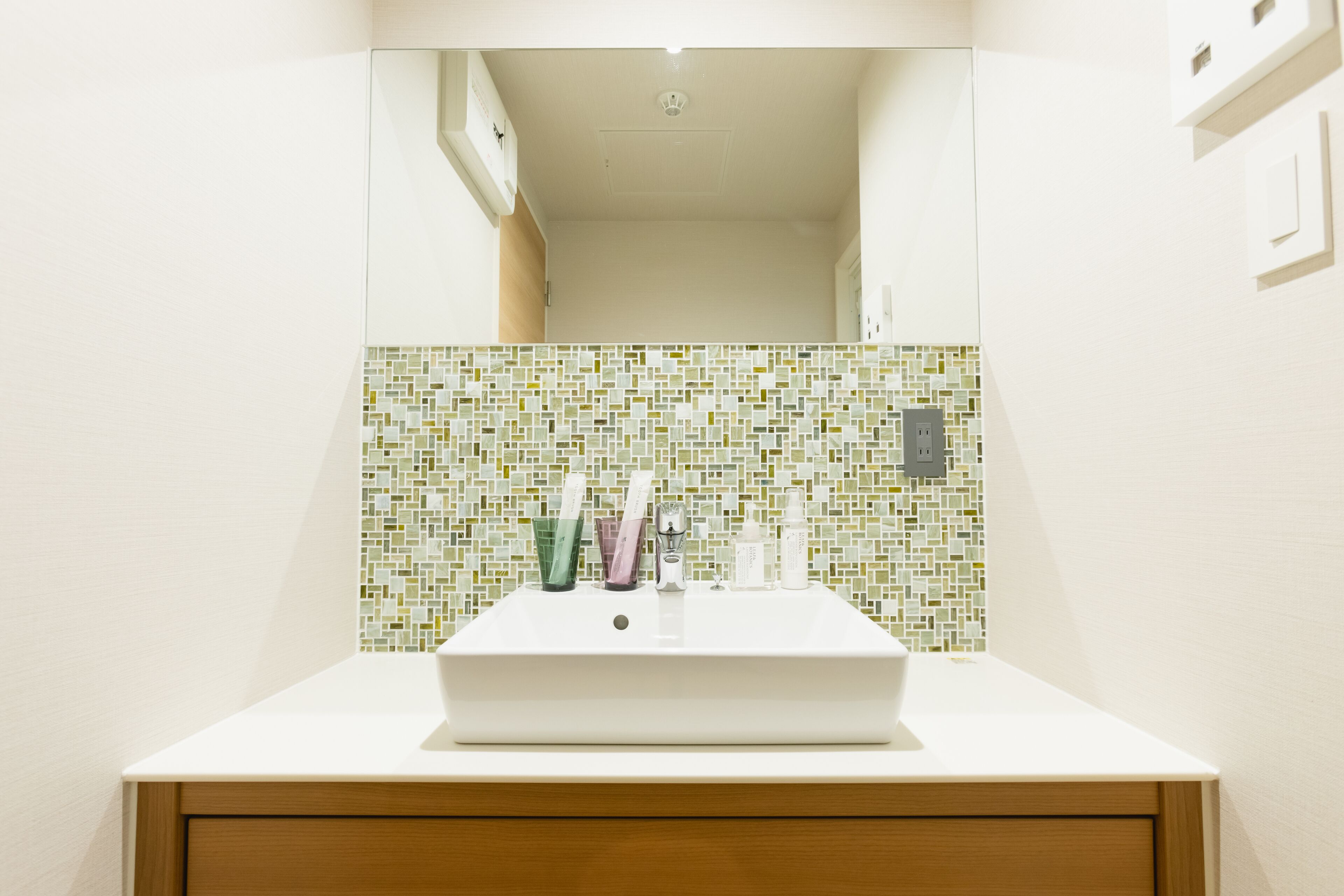 A bathroom with a white sink, a mirror, and a mosaic tile backsplash.