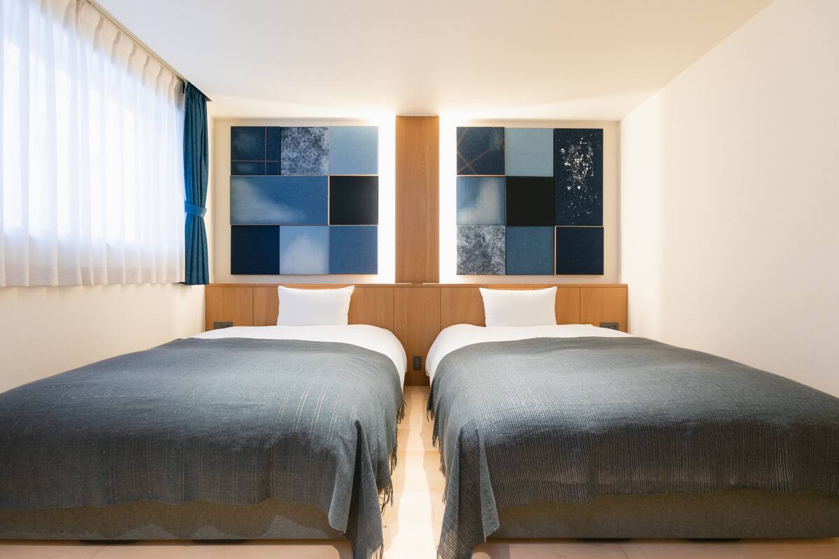 Een hotelkamer met twee bedden, een houten hoofdeinde en een raam met uitzicht op de lucht.