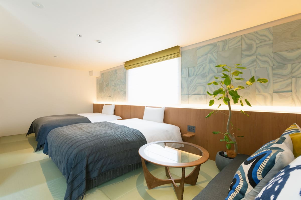 Hotelkamer met twee bedden, een klein rond tafeltje, een potplant en een groot abstract schilderij aan de muur.