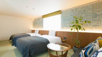 A hotel room with two beds, a small round table, a potted plant, and a large abstract painting on the wall.