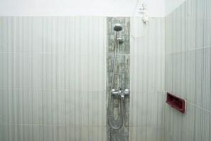 Ducha con pared de piedra, un jabonera roja y un enchufe blanco.