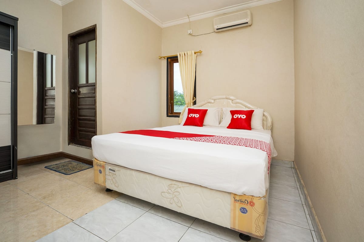 A bedroom with a bed, a door, a window with curtains, and an air conditioning unit on the wall.