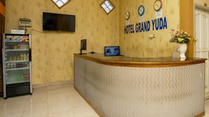 A hotel reception desk with a digital screen, a clock, and a sign reading "HOTEL GRAND YUDA". - OYO 2181 Hotel Grand Yuda (Tenggarong)