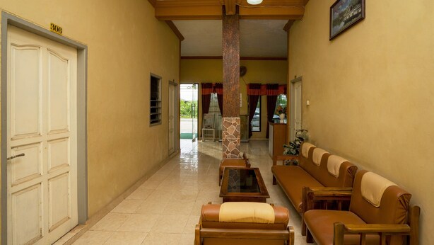 A hallway with a beige wall, a white door, a bench, and a column. - OYO 2181 Hotel Grand Yuda (Tenggarong)