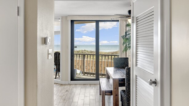 A room with a wooden table and chairs, a view of the beach through a sliding glass door, and a ceiling fan. - Sea Gull #107: Beachfront 2 Bedroom 2 Bathroom With Spectacular Views and 24 Hour Management (Port Aransas)