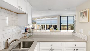 A modern kitchen with white cabinets, stainless steel sink, and a view of the beach through large windows. - Sea Gull #107: Beachfront 2 Bedroom 2 Bathroom With Spectacular Views and 24 Hour Management (Port Aransas)