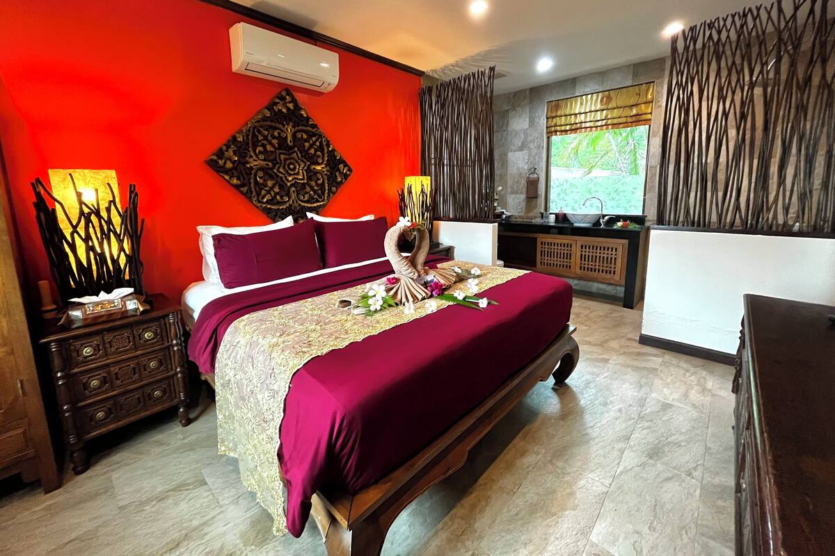 A hotel room with a large bed, a nightstand, a dresser, a vanity, and a window with curtains.