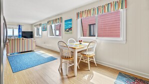 A dining area with a wooden table, white chairs, and colorful curtains. - Inlet Pointe Villas 14E-Oceanfront 2BR- Pool (North Myrtle Beach)