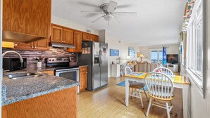 A modern kitchen with granite countertops, wooden cabinets, stainless steel appliances, and a dining area with a wooden table and chairs. - Inlet Pointe Villas 14E-Oceanfront 2BR- Pool (North Myrtle Beach)