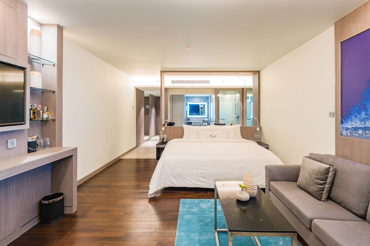 Una habitación de hotel moderna con una cama grande, un sofá, un televisor y un minibar.
