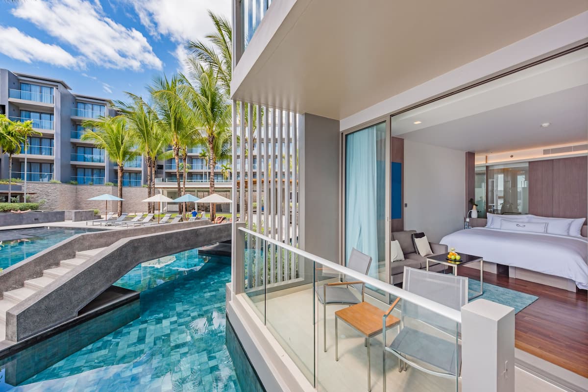 Habitación de hotel moderna con balcón que da a una piscina, una cama y un pequeño rincón de descanso.