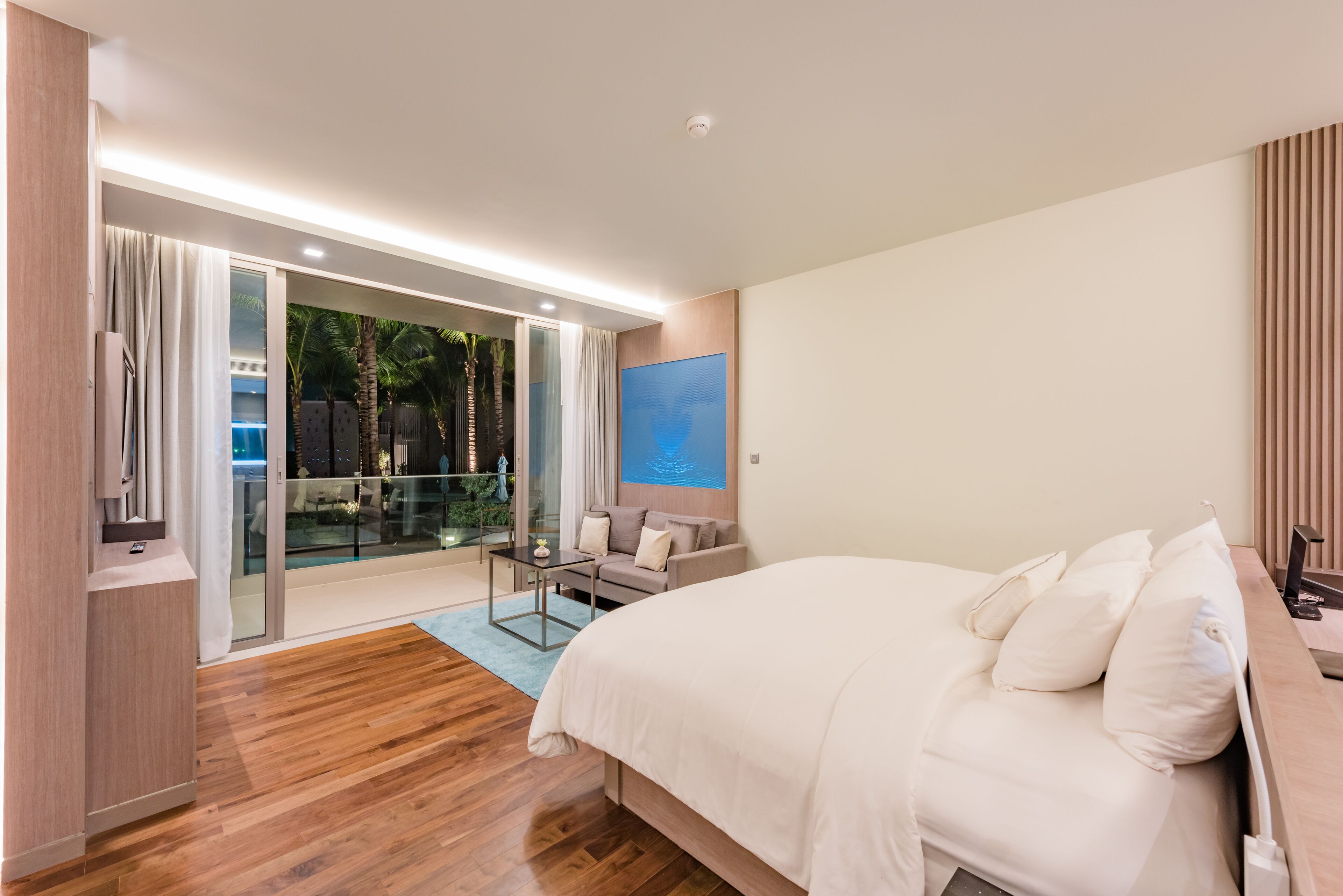 Un dormitorio moderno con una cama grande, una puerta de vidrio que da a un balcón y un televisor de pantalla plana.