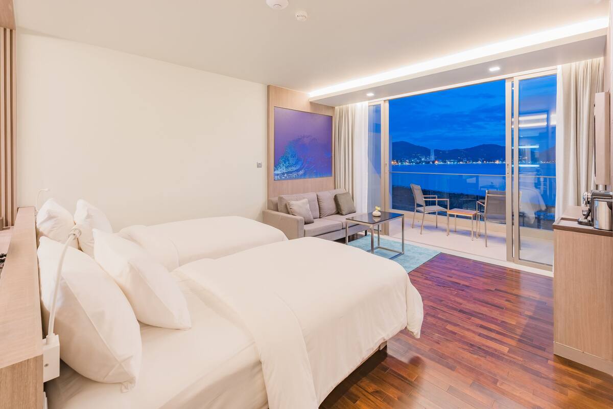 Una habitación de hotel moderna con una cama grande, un sofá, una mesita y un balcón con vistas a la ciudad.