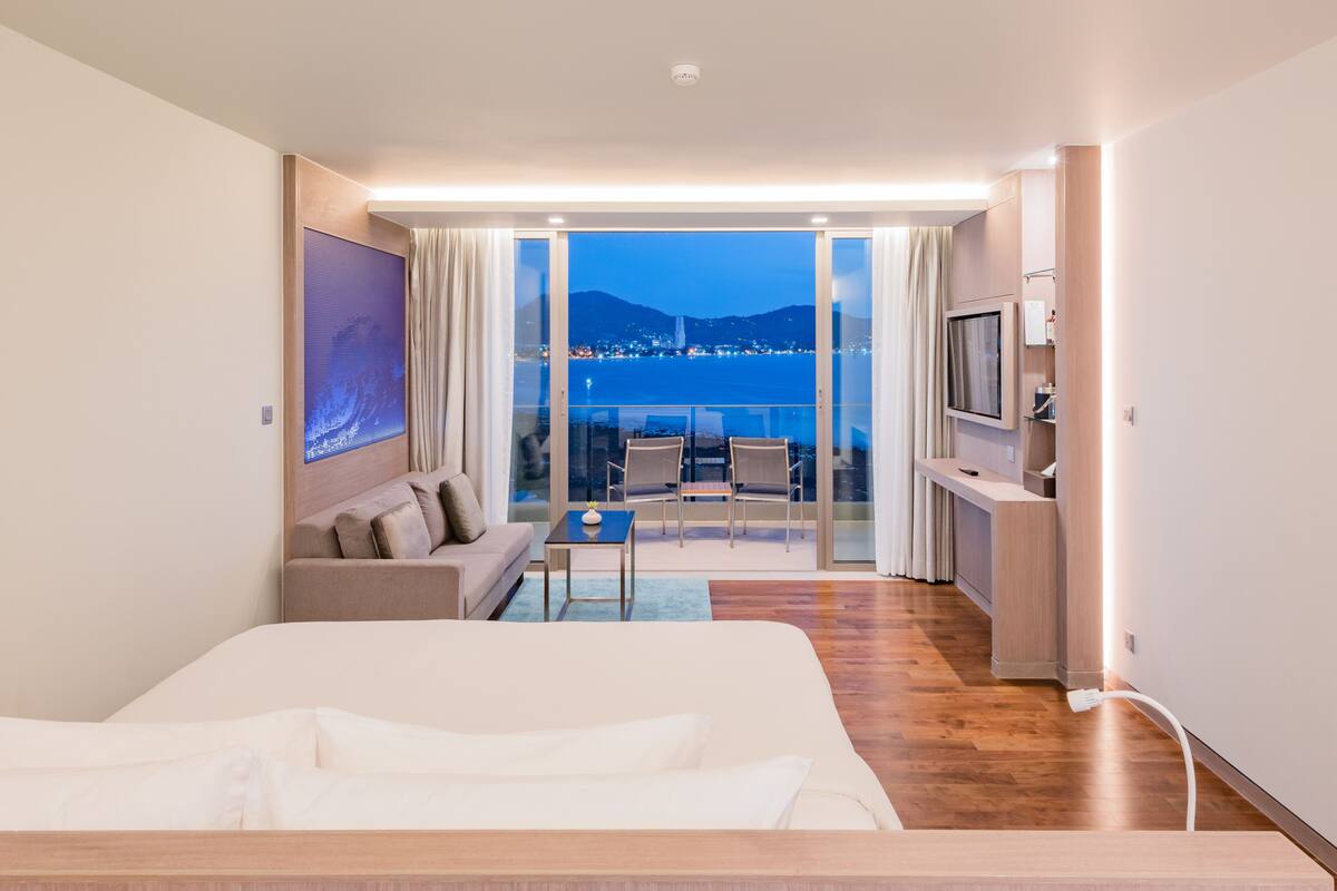 Una habitación de hotel moderna con una cama grande, un sofá, una mesita y un balcón con vistas a la ciudad.