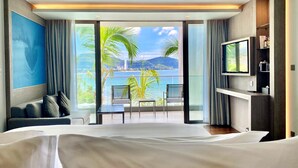 A hotel room with a large bed, a TV, and a balcony with a view of the sea and mountains. - Oceanfront Beach Resort (Patong)