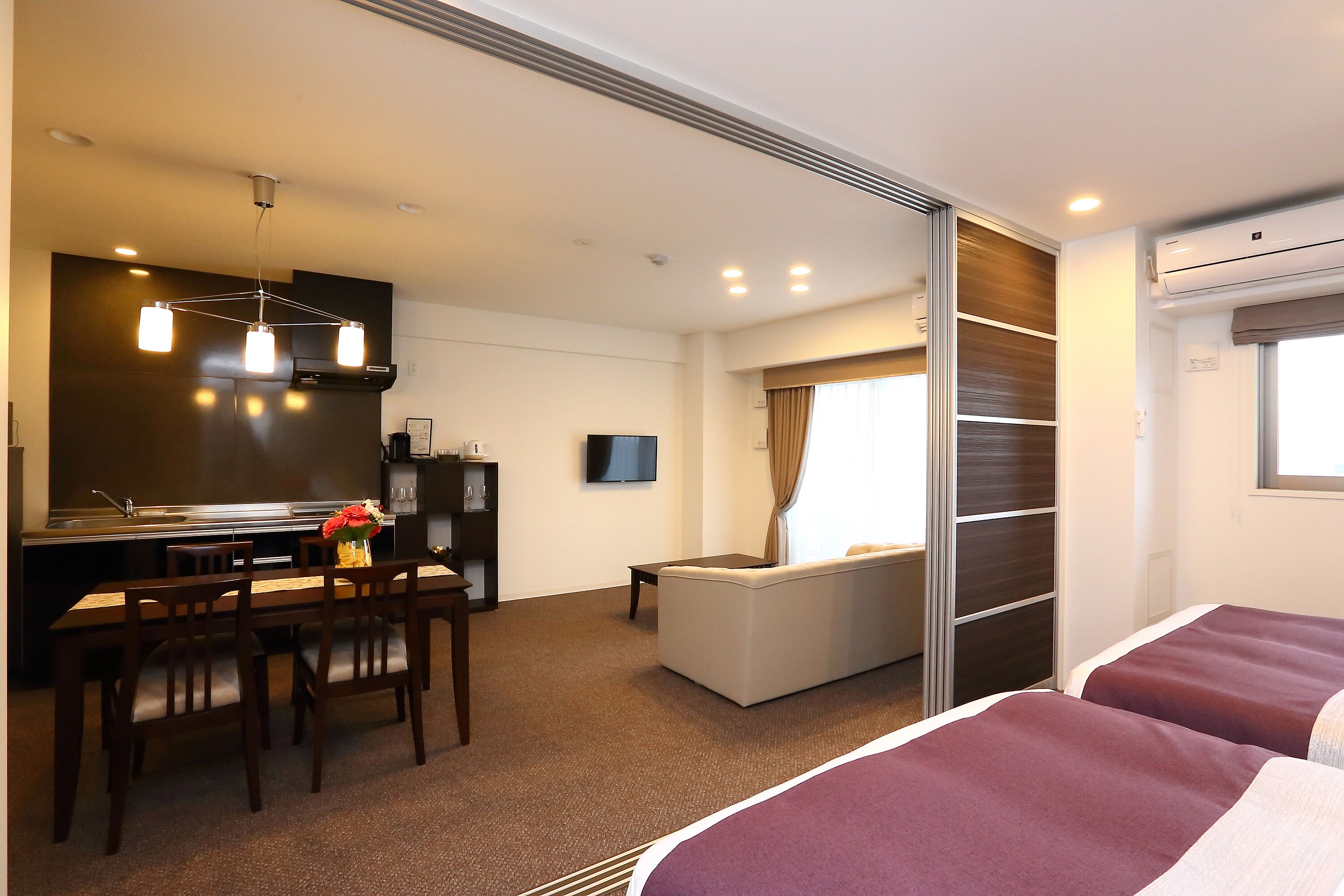 Une chambre d’hôtel comprenant un lit, un canapé, un coin repas avec une table et des chaises, une télévision et une kitchenette.