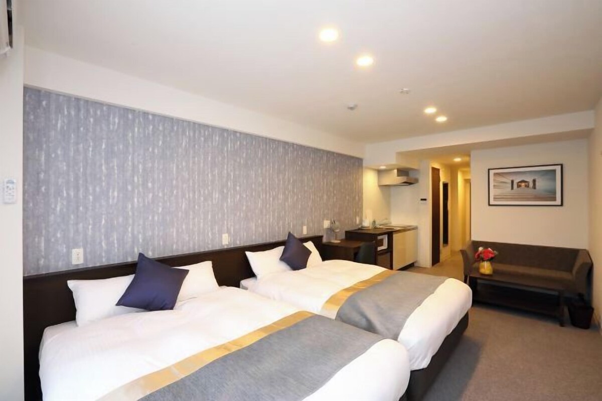 Habitació d'hotel amb dos llits, un escriptori, un sofà i una fotografia encadrada a la paret.
