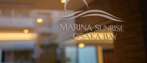 Un logo avec le texte « MARINA SUNRISE OSAKA BAY » sur une surface de verre.