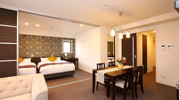 A hotel room with a bed, bedside tables, a dining table with chairs, a sofa, and a hallway leading to another room.