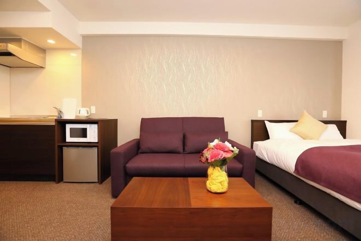 Une chambre d’hôtel comprenant un lit, un canapé, une table basse avec un vase, un four à micro-ondes et un petit réfrigérateur.