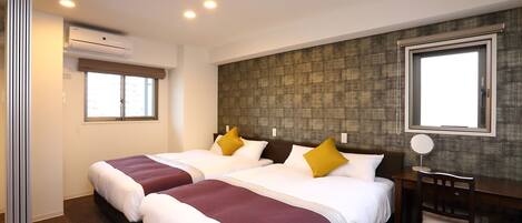 A hotel room with two beds, a desk, a chair, and an air conditioning unit.