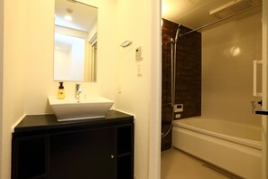 Une salle de bain avec un lavabo blanc, un meuble-lavabo noir, un miroir, une douche et une baignoire.