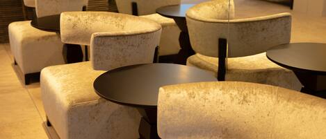 A seating area with cushioned chairs and round tables, arranged in a modern indoor setting.