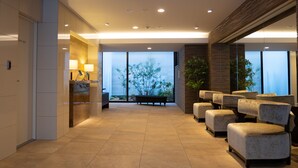 Een moderne lobby met een receptiebalie, een zithoek en grote ramen met uitzicht op het omliggende landschap.