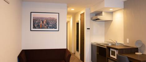 Una habitación de hotel compacta con sofá, una pequeña mesa, kitchenette y un cuadro con una vista de la ciudad.