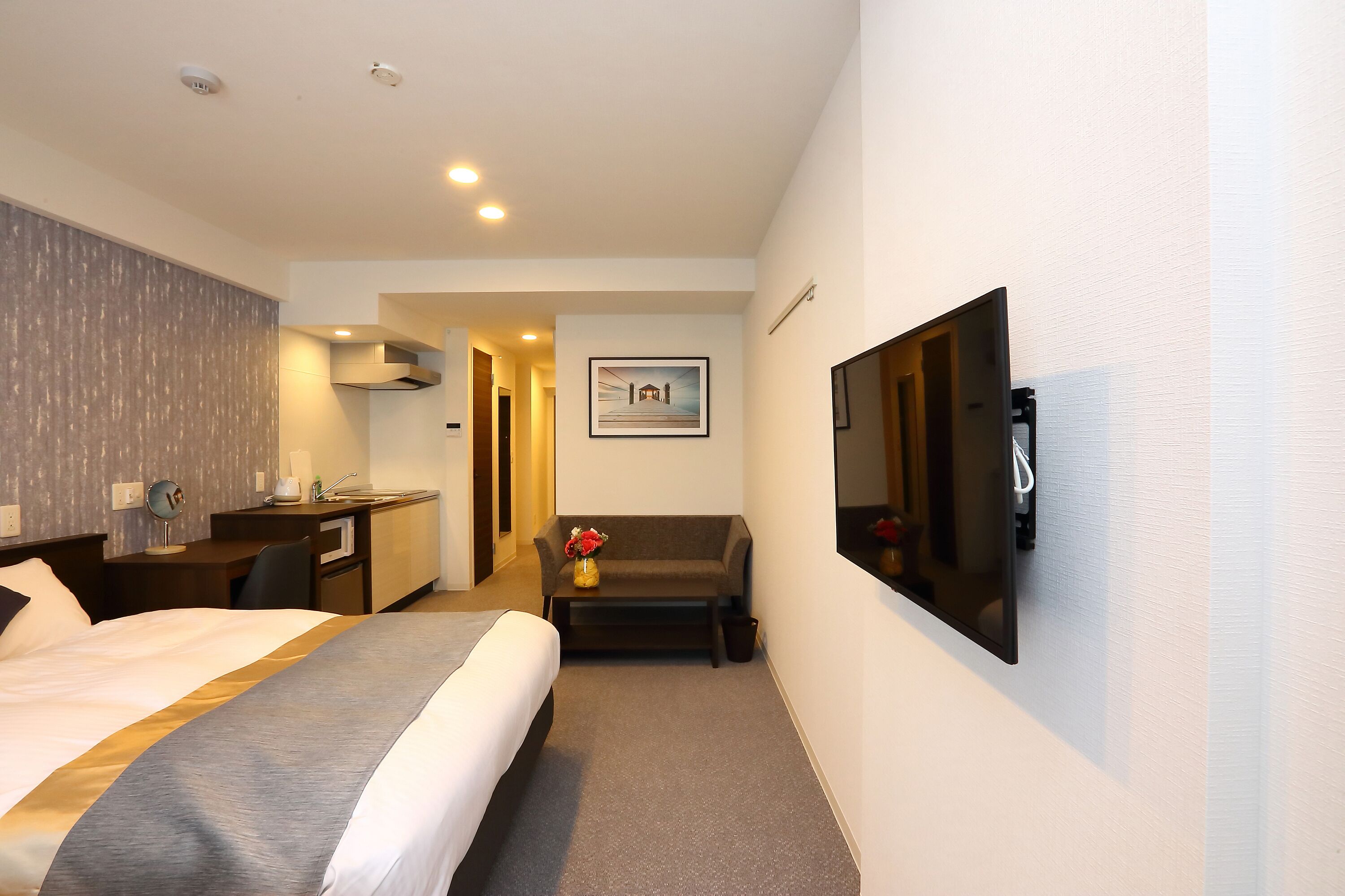 A hotel room with a large bed, a desk, a sofa, a TV, and a picture on the wall.